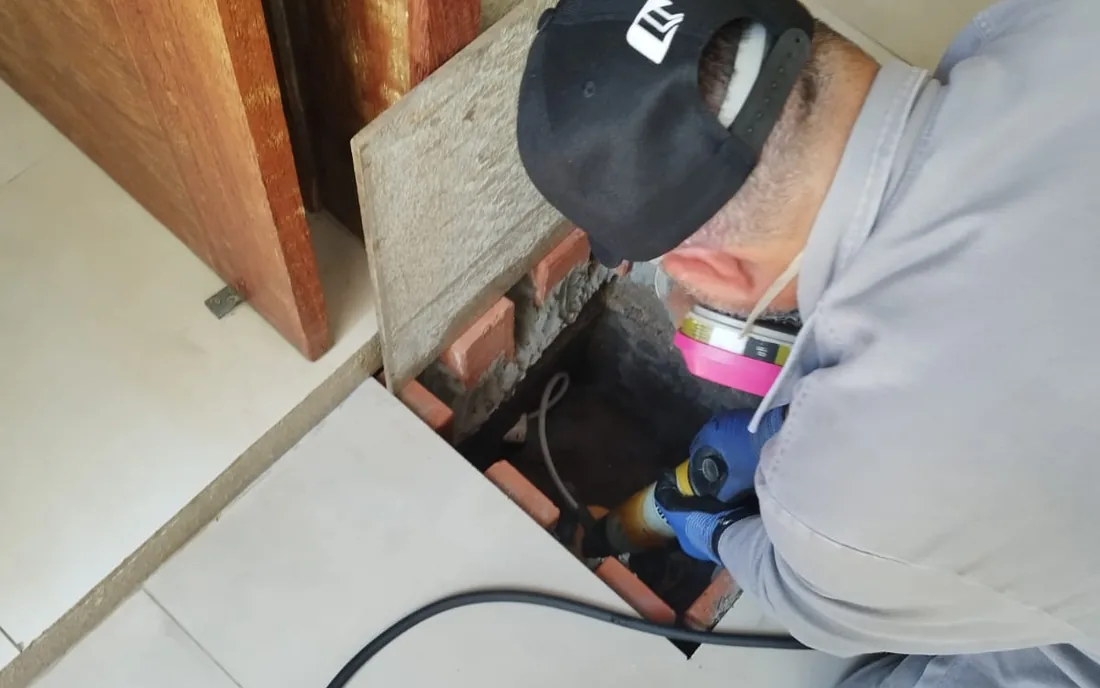 Técnico com respirador e luvas injetando produto no vão do piso, durante uma barreira química de solo.